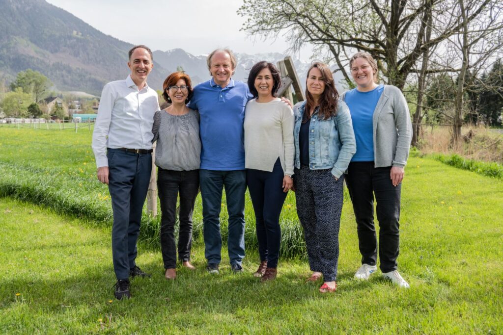 Six LED team members stand together outdoors in a green field with mountains behind them