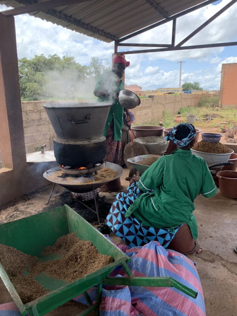 Frauen kochen unter einem überdachten Bereich mit großen Töpfen und Getreide.