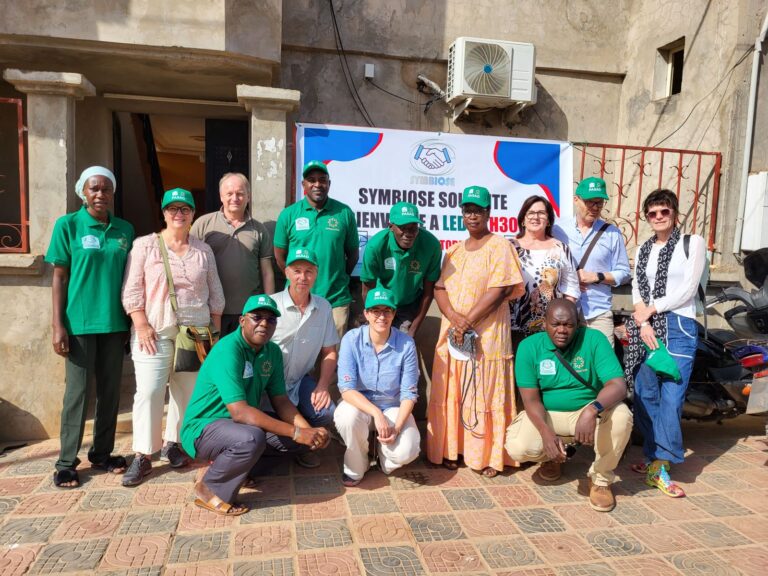 Gruppe von Menschen vor einem Gebäude mit Banner, einige tragen grüne Hemden und Mützen