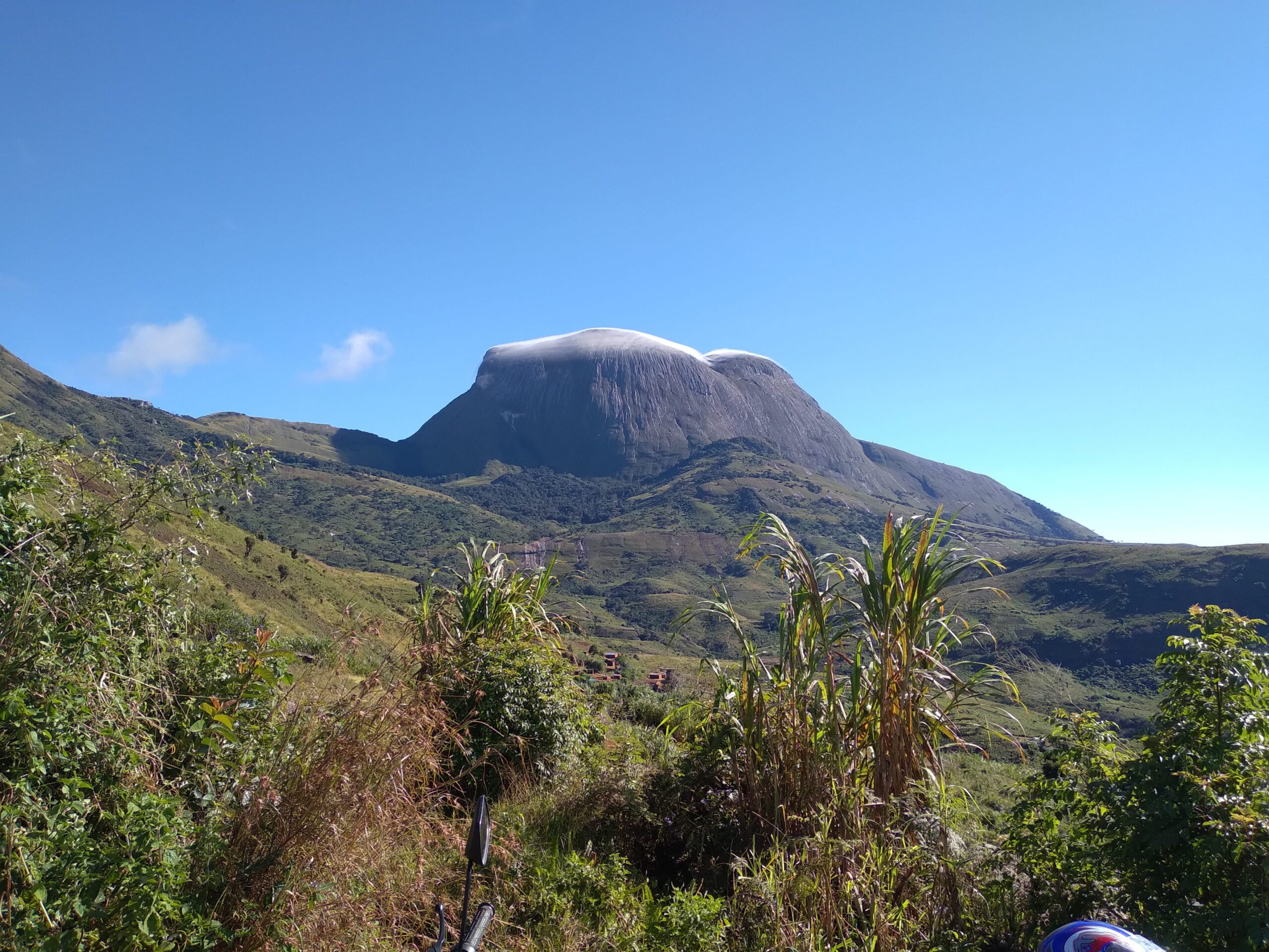 Green mountain landscape with a rounded rocky peak under a clear blue sky