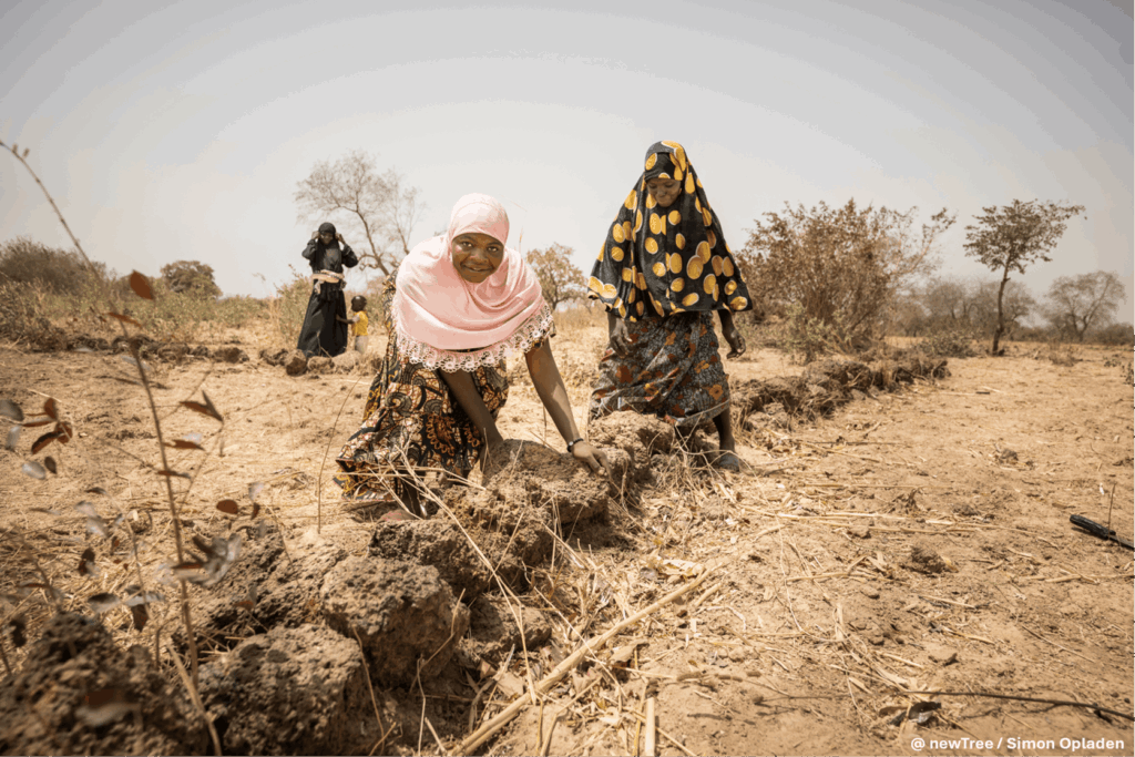Women in headscarves work in a dry field, building soil ridges for farming