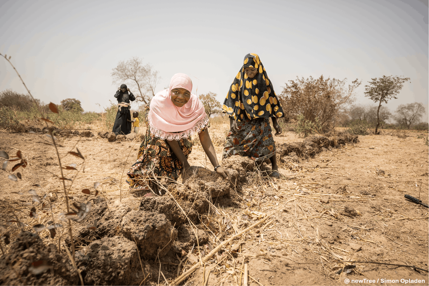 Women in headscarves work in a dry field, building soil ridges for farming