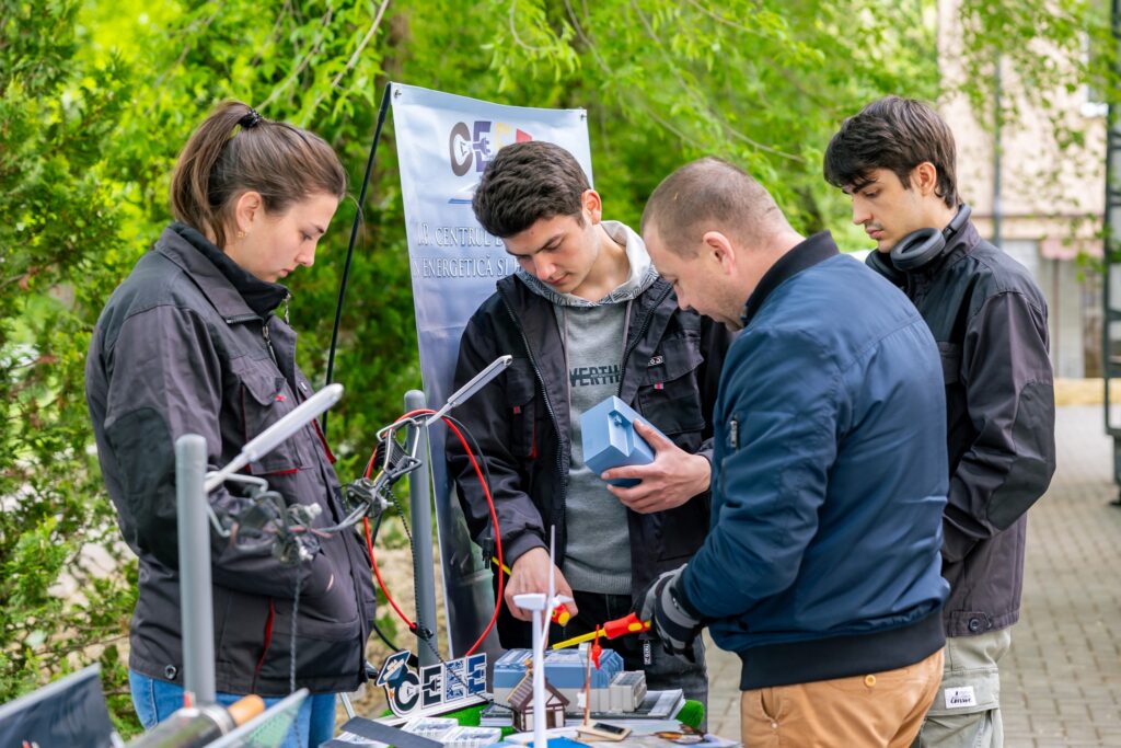 Four people examine a renewable energy model at an outdoor demonstration booth
