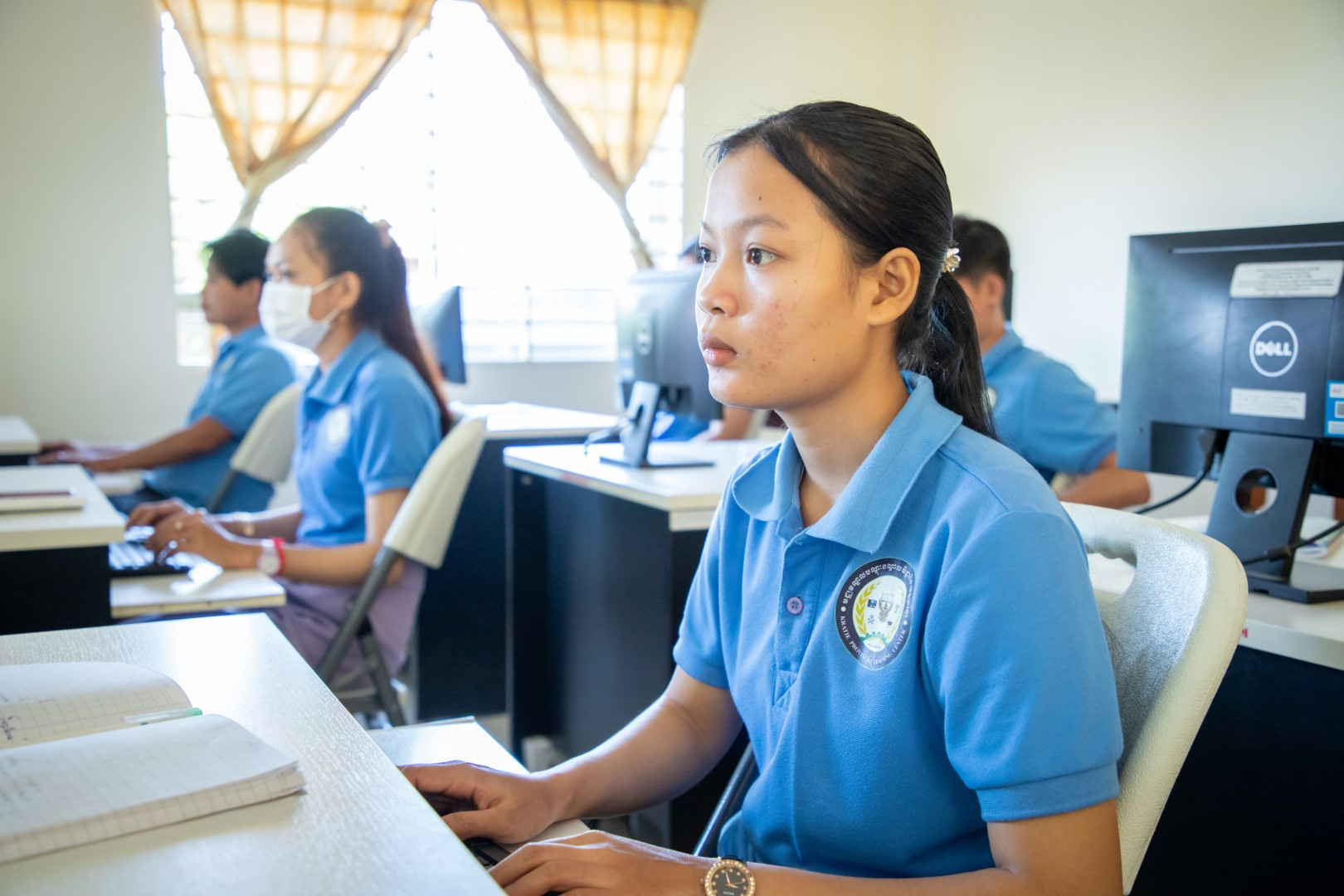 Students in blue uniforms use desktop computers in a classroom training session.