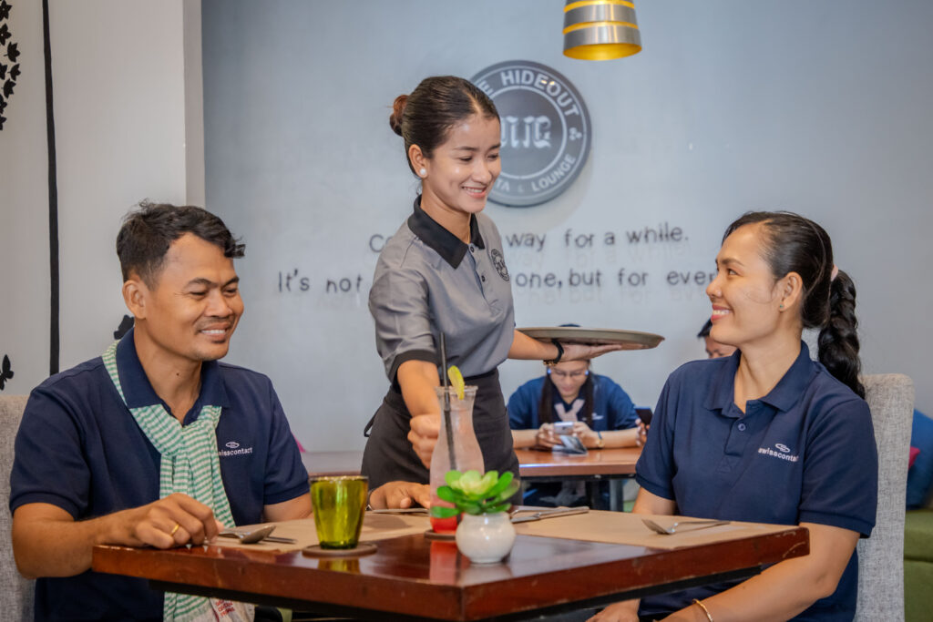Waitress serves drink to smiling guests in restaurant