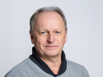 Portrait of an older man with a gray sweater against a light background