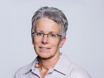 Portrait of a woman with glasses and short gray hair against a light background