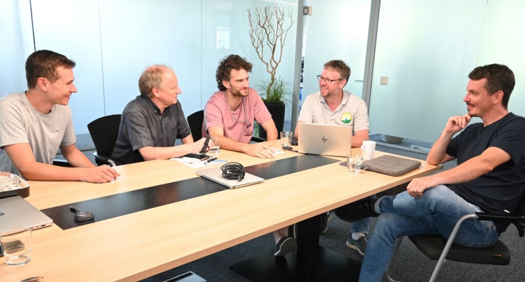 Five men in a meeting room discussing development work around a conference table