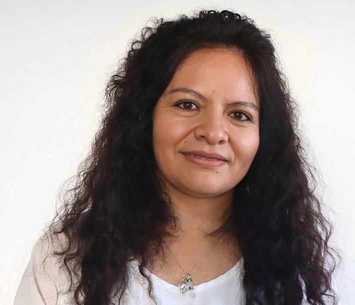 Woman with curly hair and white top in front of a neutral background