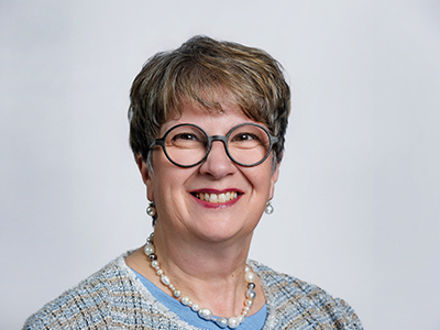 Smiling woman with glasses and pearl necklace against a light background