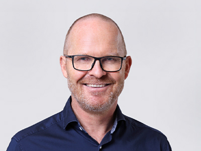 Smiling man with glasses and blue shirt against a light background