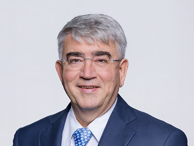 Porträt eines älteren Mannes im Anzug mit Brille vor hellem Hintergrund