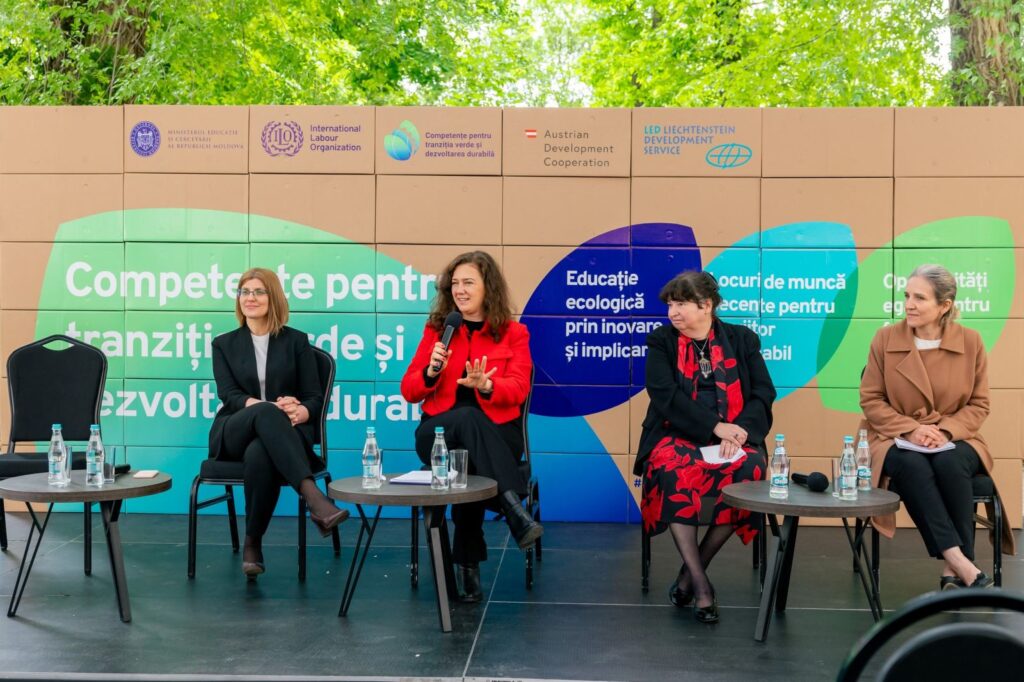 Four women discuss on a stage in front of a colorful wall of logos.