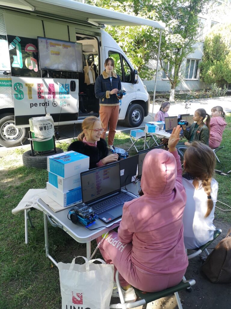 Children learn coding and robotics beside a mobile STEM workshop van outdoors