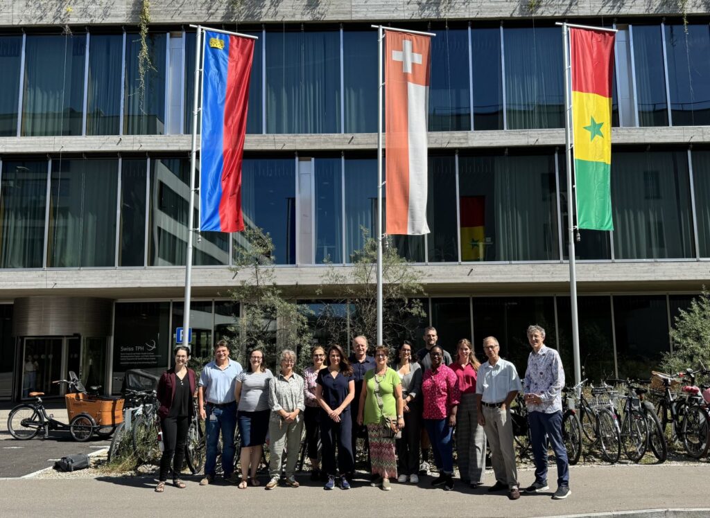 Group of professionals standing outside a modern building beneath Liechtenstein, Swiss, and Senegal flags