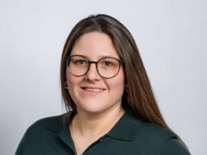 Porträt einer lächelnden Frau mit Brille vor hellem Hintergrund