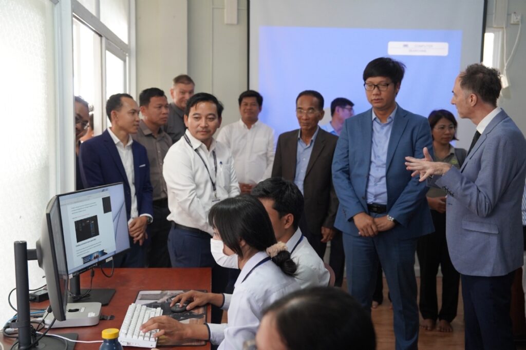 LED delegation observes a computer demonstration during a formal project visit in an office