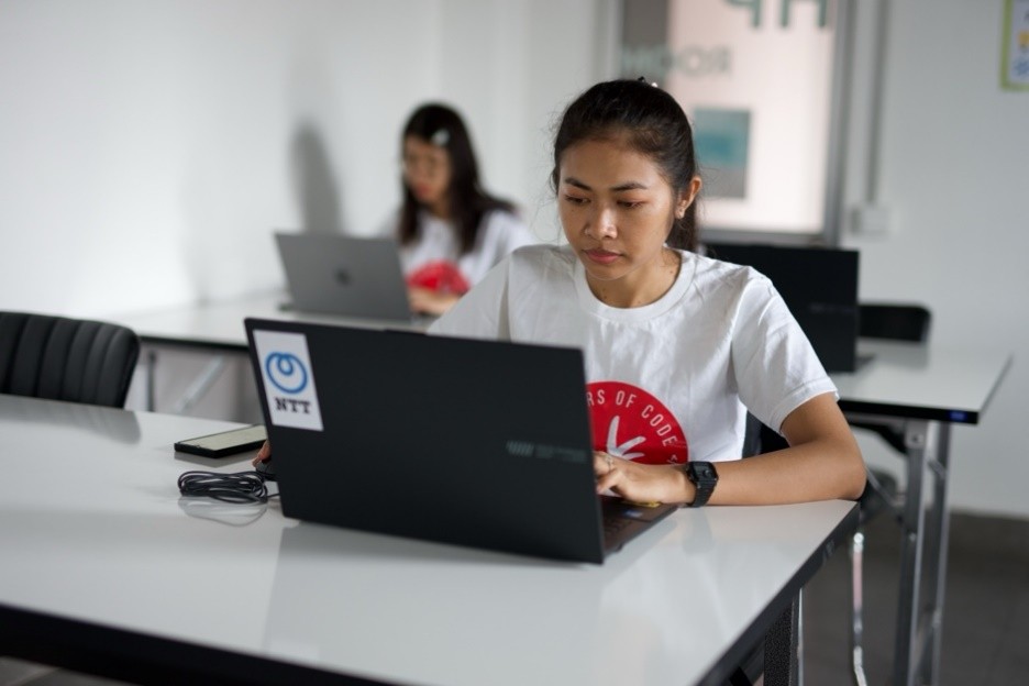 Woman working on a laptop in a classroom, with another participant using a laptop behind her