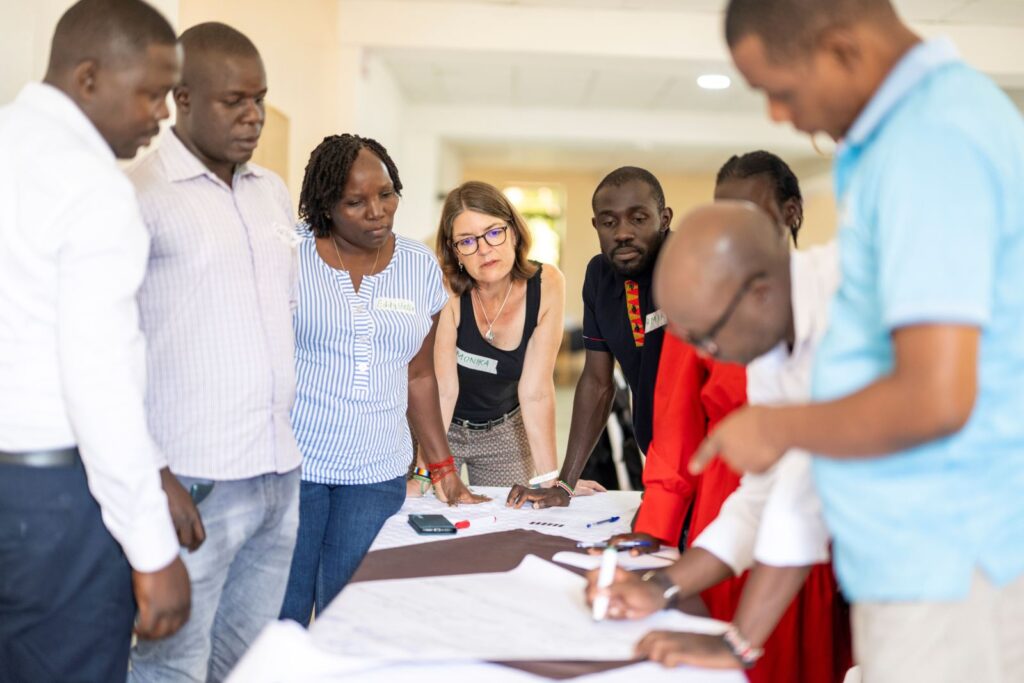 Diverse LED workshop participants gather around a table, reviewing notes and planning together