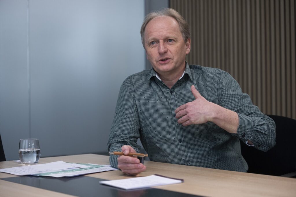 Man speaking at a meeting table with papers, pen, and water glass in an office