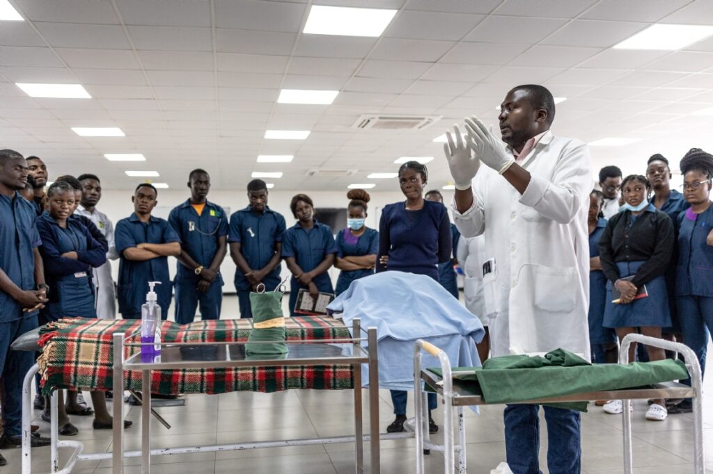 Medical trainer in white coat demonstrates hand hygiene to students in a clinical training room