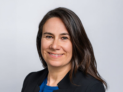 Porträt einer lächelnden Frau mit dunklem Haar vor hellem Hintergrund