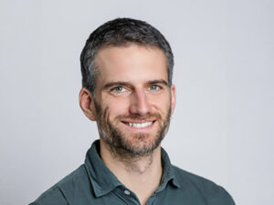 Lächelnder Mann mit kurzem Haar und Bart vor hellem Hintergrund