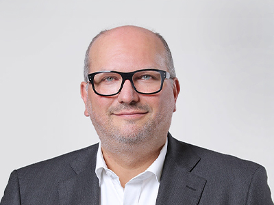 Porträt eines Mannes mit Brille im grauen Anzug vor hellem Hintergrund