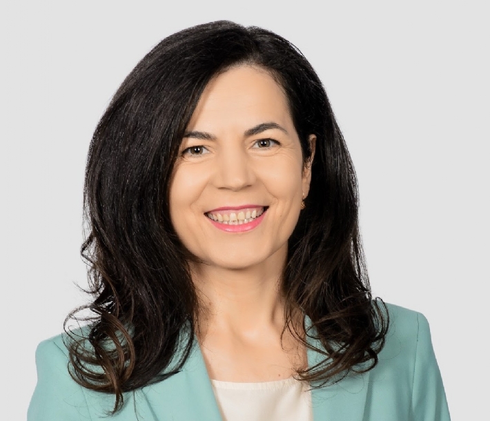 Geschäftsfrau mit dunklem Haar in türkisfarbenem Blazer lächelt freundlich