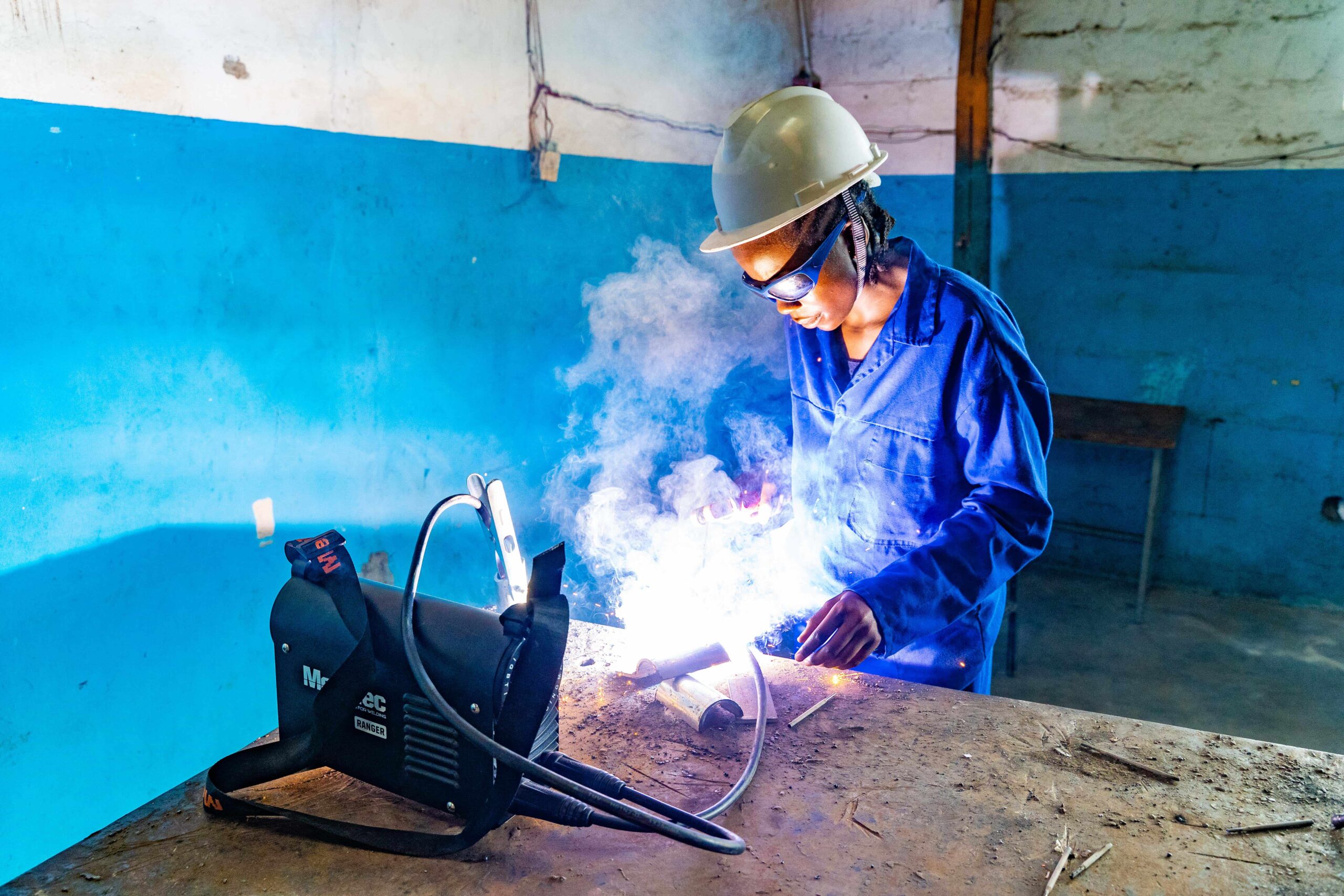 Schweißerin mit Schutzhelm und Brille arbeitet in Werkstatt