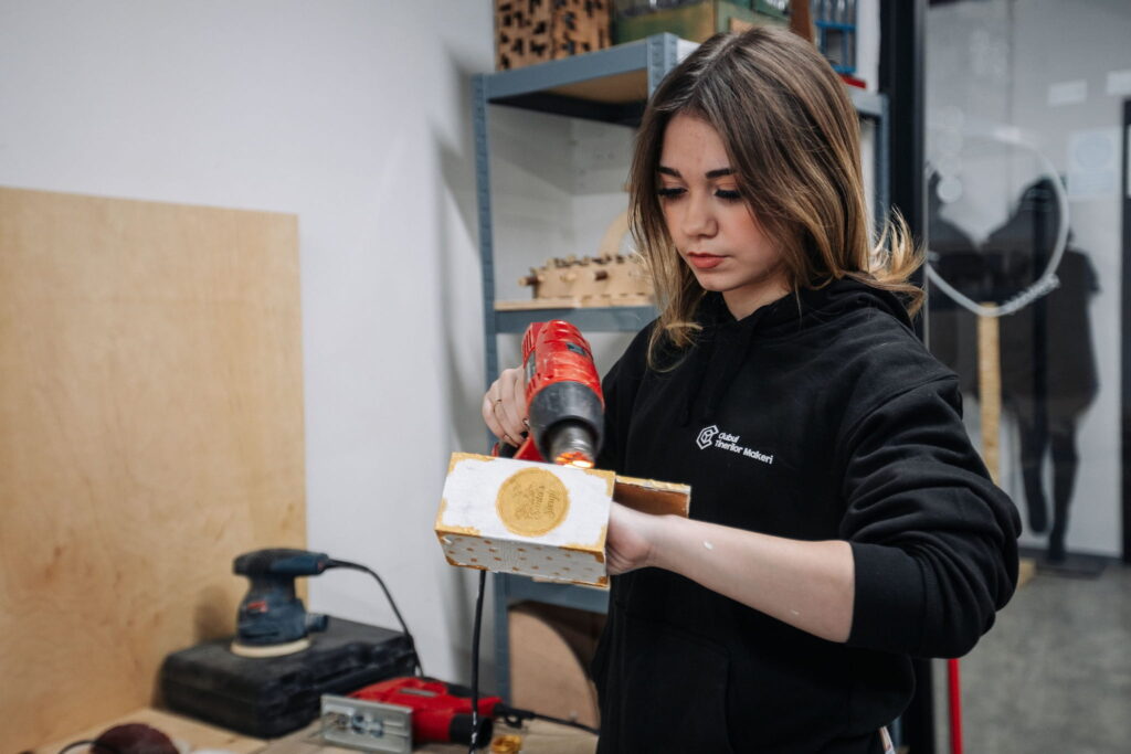 Junge Frau arbeitet mit Heißluftpistole an Holzprojekt in Werkstatt