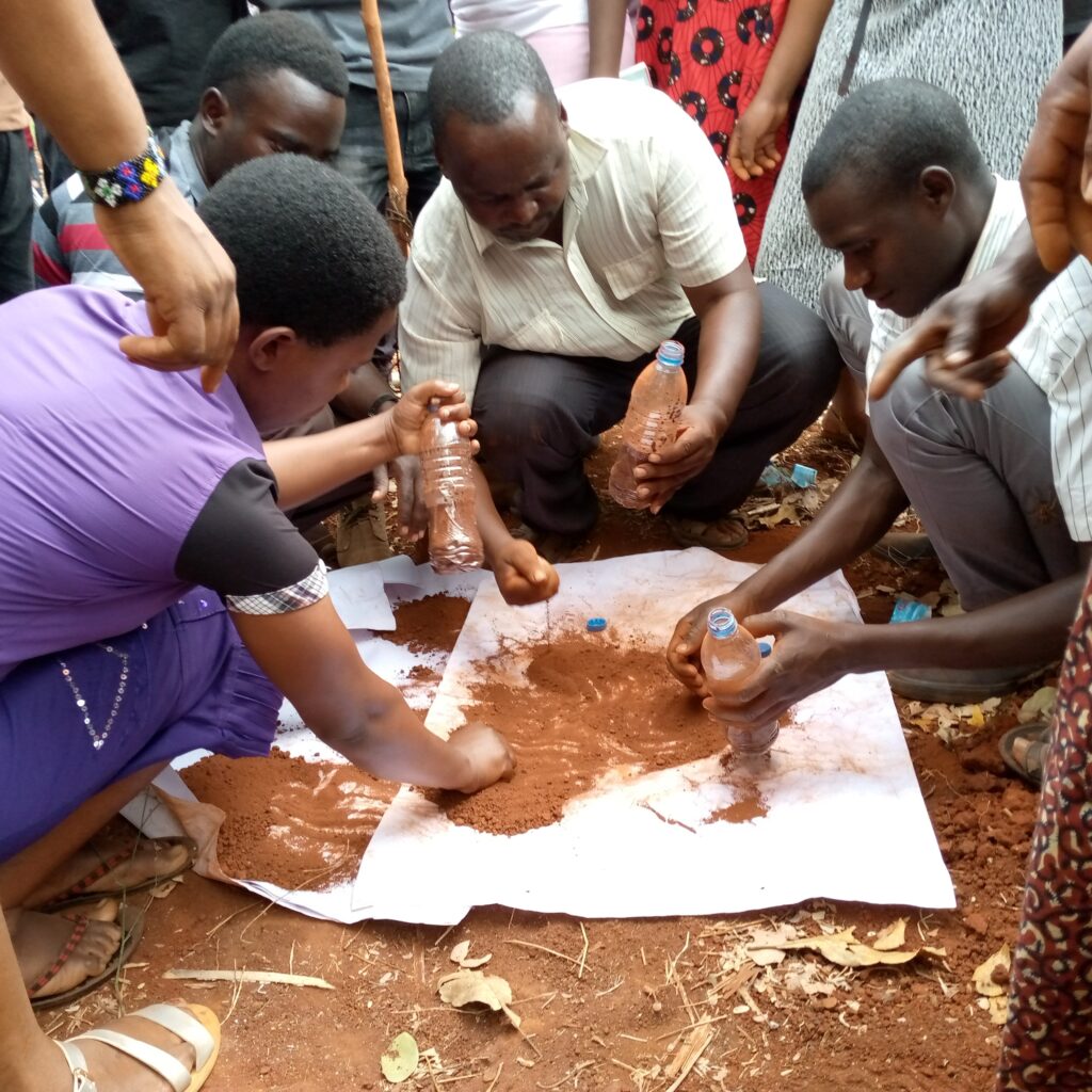 Group of people kneel around soil samples on paper, using plastic bottles in a field exercise.