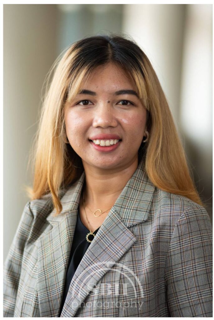 Junge Frau mit hellgrauem Blazer, lächelt in die Kamera